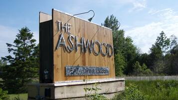 A wooden sign with "The Ashwood" and "EAT DRINK SLEEP" text, surrounded by greenery.