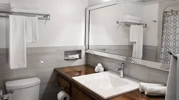A modern bathroom with a white sink, wooden vanity, a toilet, and a large mirror.