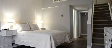 A bedroom with a bed, nightstands, a rug, a staircase, and a door leading to another room.