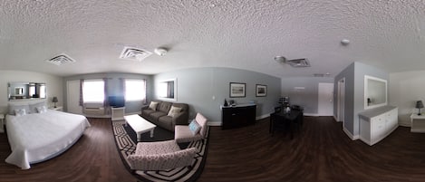 Amplia habitación de hotel con una cama grande, un sofá, una mesa de comedor y un televisor.