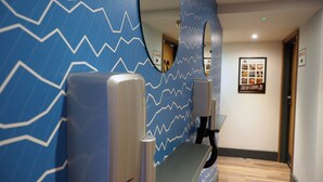 Un espace d’accueil d’hôtel avec un mur à motifs bleus, un comptoir d’accueil, un miroir et une affiche informative encadrée accrochée au mur.