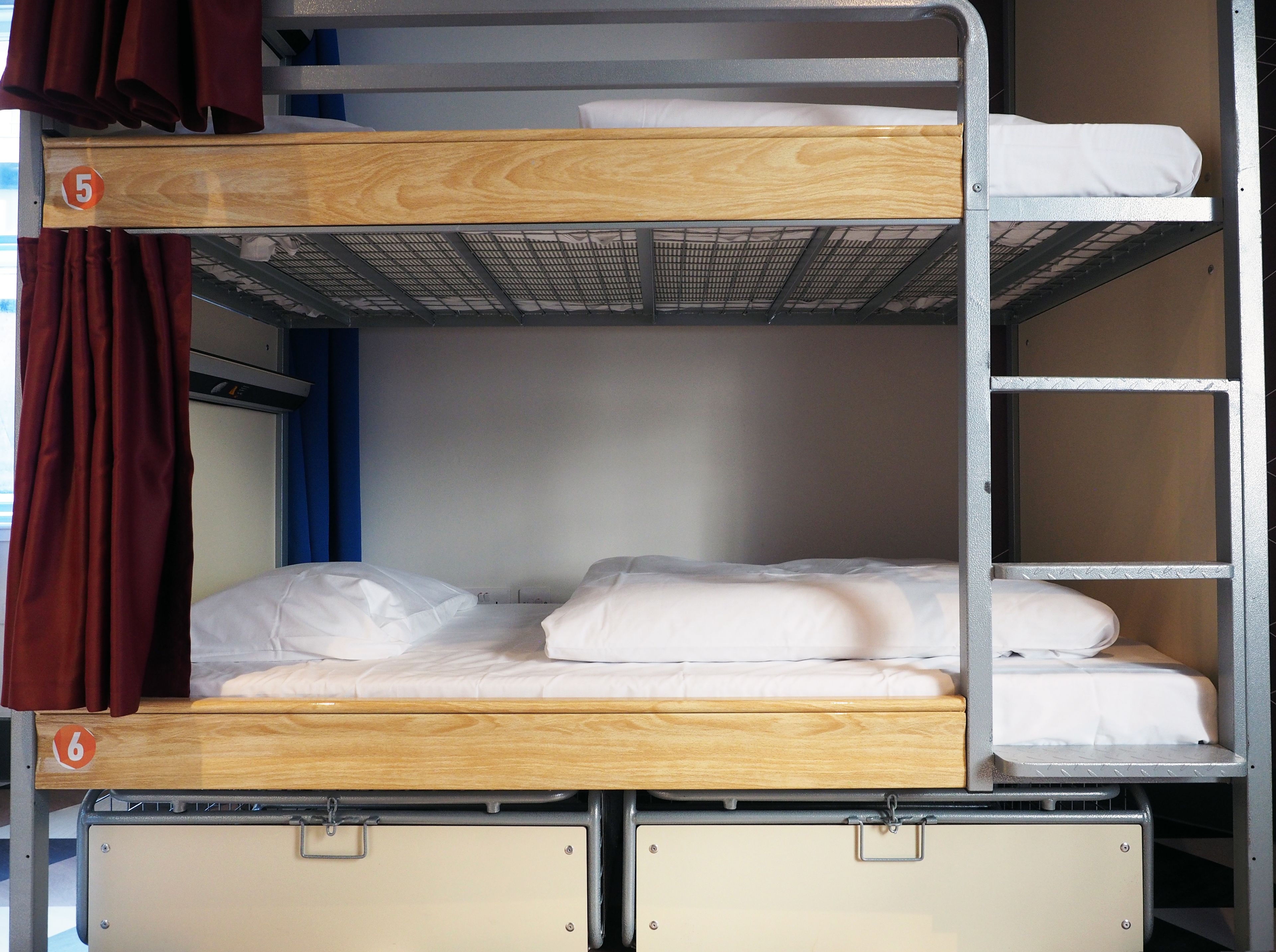 Uma cama beliche com dois níveis, cada um com colchão e travesseiros. Há duas divisórias para guardar objetos na parte inferior.