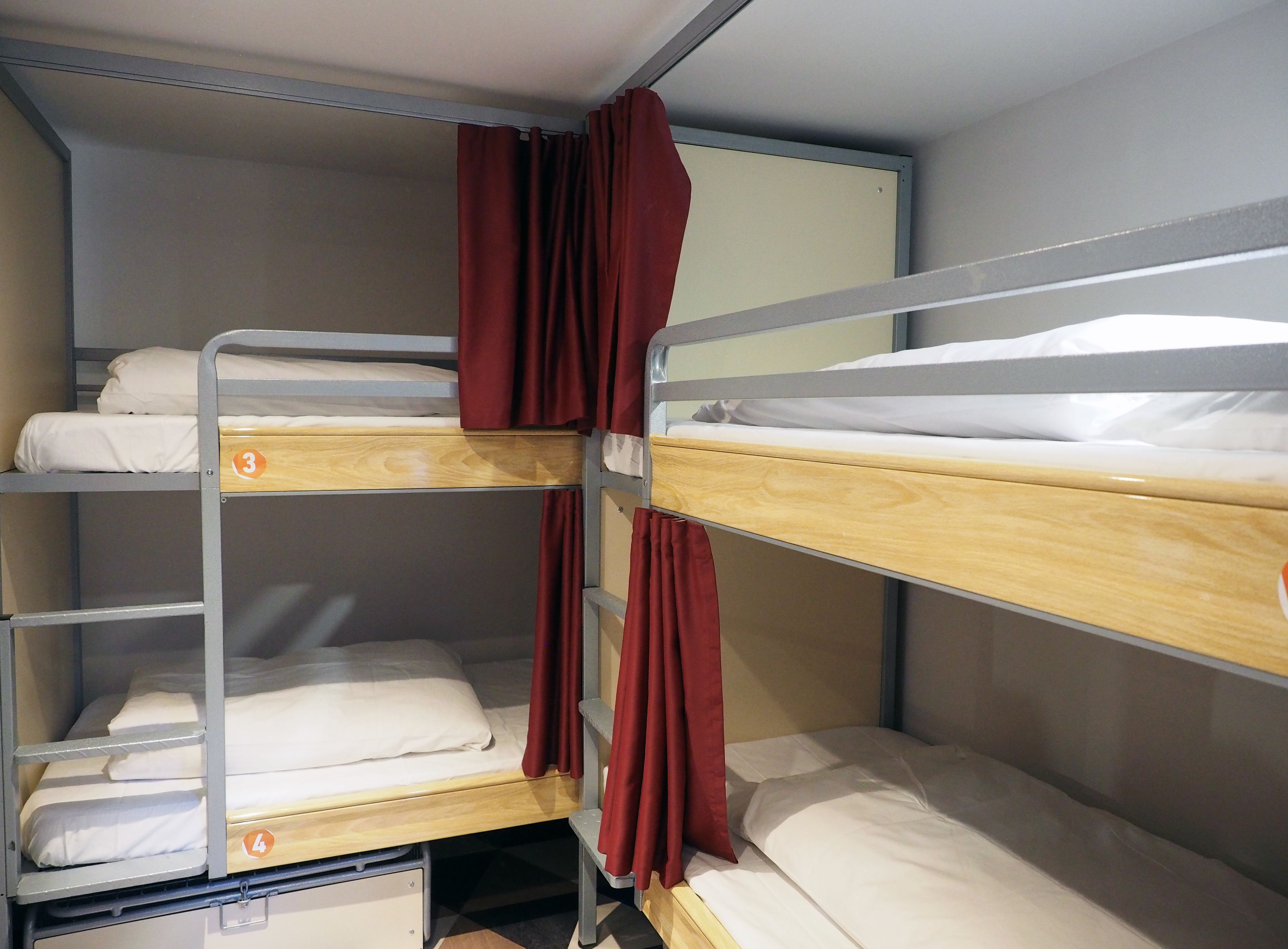 A bunk bed room with three levels, each with a wooden frame and white bedding.