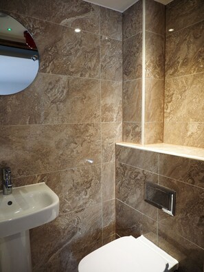 A bathroom with a marble wall, a sink, and a toilet. - St Christopher's Liverpool Street - Hostel (London)