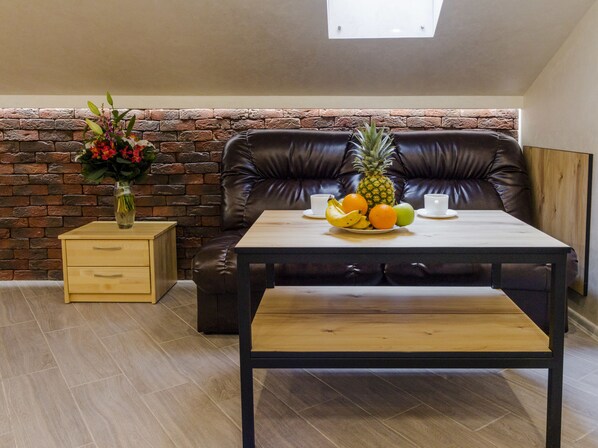 Un rincón acogedor con una pared de ladrillo, una mesa de madera con fruta y un jarrón de flores.