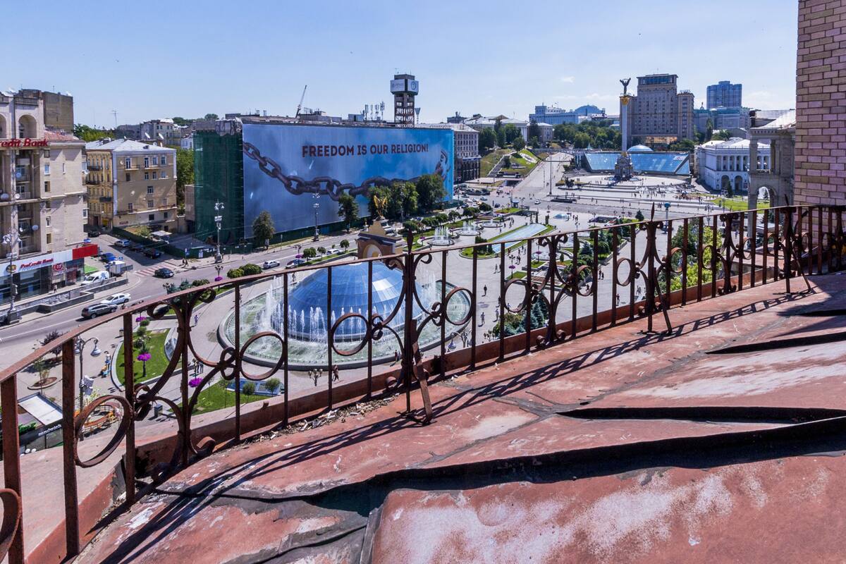 A cityscape with a large fountain, a prominent Freedom is Our Religion billboard, and a view of a historic building.