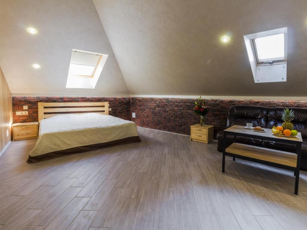 A bedroom with a sloped ceiling, a bed, a wooden bench, a small table with fruit, and a brick accent wall.