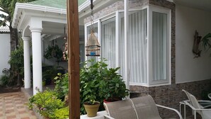 A covered outdoor seating area with a white chair and a table, surrounded by potted plants and a hanging birdcage. - Hospedaje Solymar Islas (San Andrés)