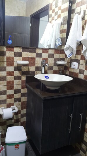 Casa de banho com painel de azulejos xadrez, lavatório branco com autocolante azul, espelho e toalheiro com várias toalhas.