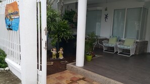 Uma área externa coberta com cerca branca, duas cadeiras, um vaso de planta e uma placa com a inscrição 'Solmujislas Apartamentos'.
