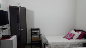 Um quarto com cama, cadeira, guarda-roupa, televisão e uma pequena mesa.