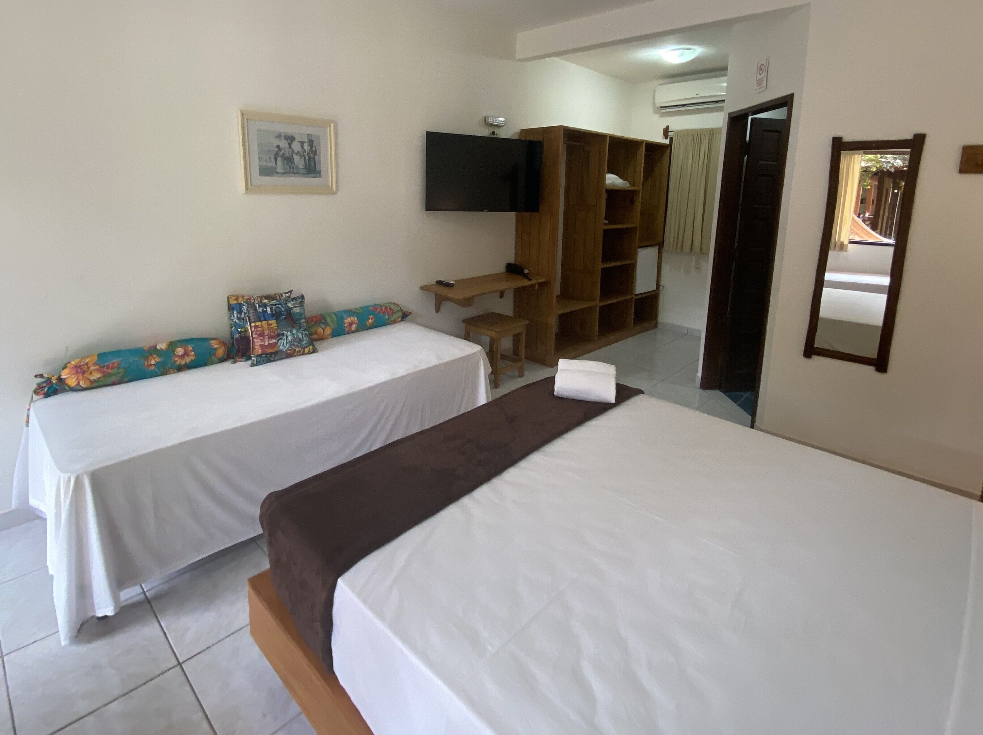 A hotel room with two beds, a TV, a wooden wardrobe, and a desk.