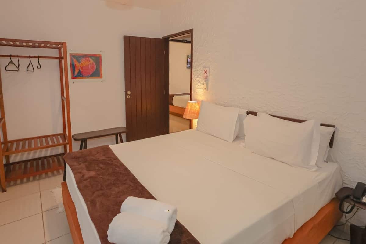 A bedroom with a bed, a wooden shelf unit, a bench, a wall-mounted lamp, and a door.