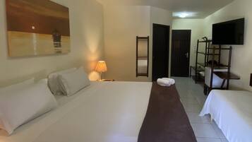 A hotel room with a large bed, a bedside lamp, a TV, a mirror, and a shelf with a chair.