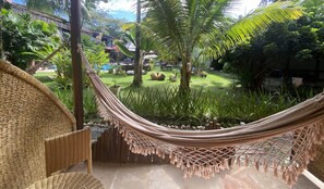 A hammock in a lush garden with a pool and outdoor furniture. - Pousada Saudosa Maloca (Porto Seguro)