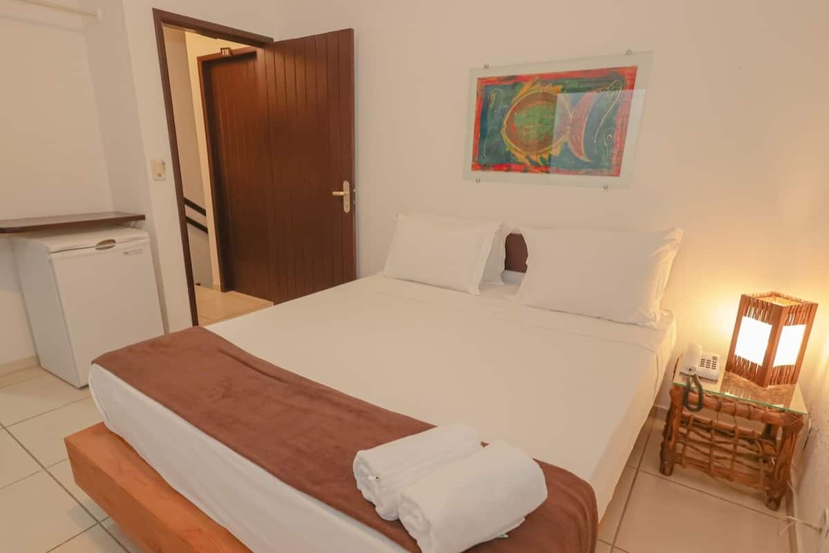 A hotel room with a bed, a small table with a lamp, and a painting on the wall.
