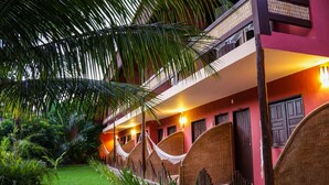 A hotel with a red facade, a balcony with wicker furniture, and a well-maintained garden. - Pousada Saudosa Maloca (Porto Seguro)
