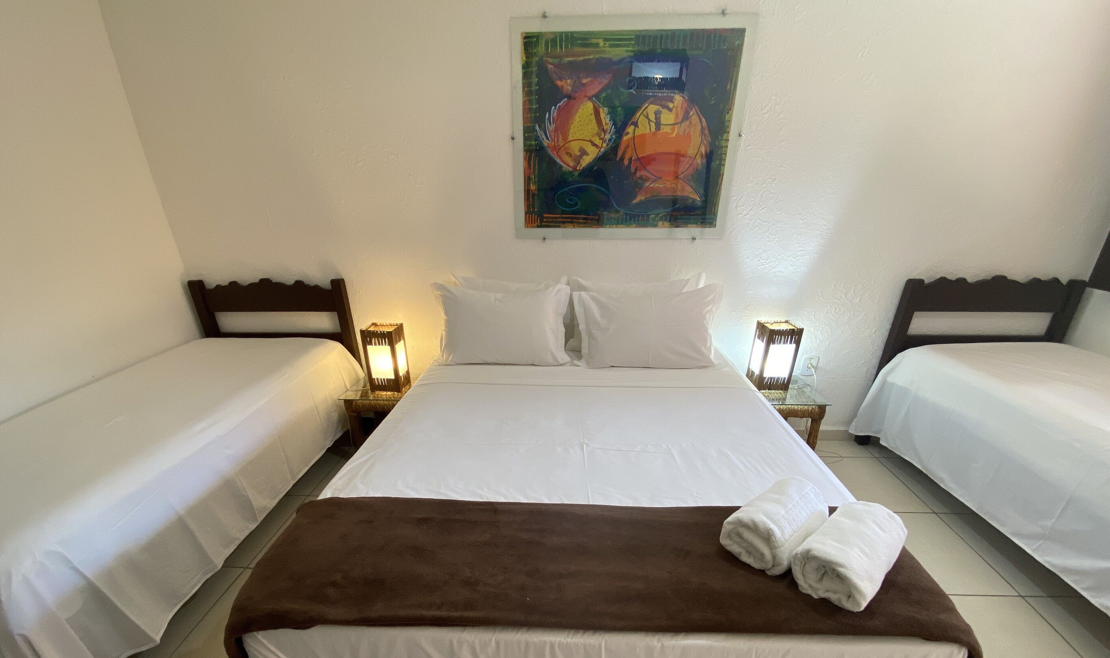 Una habitación doble con dos camas individuales, una cama grande con una manta marrón y un cuadro sobre las camas.
