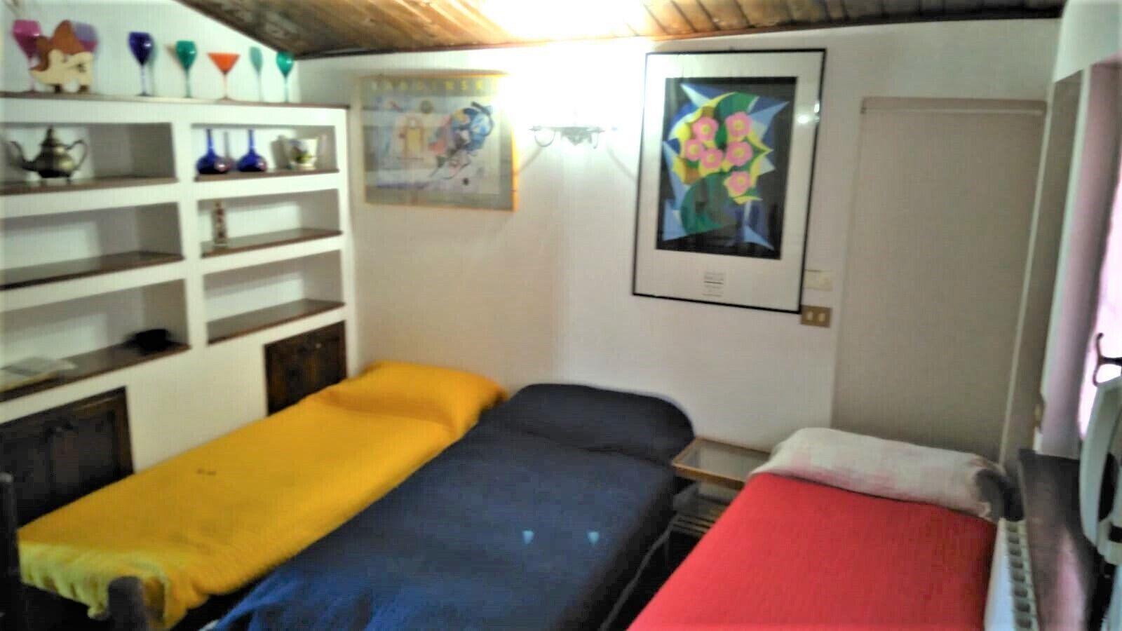 A small room with two beds, a shelf with decorative items, and a framed picture on the wall.