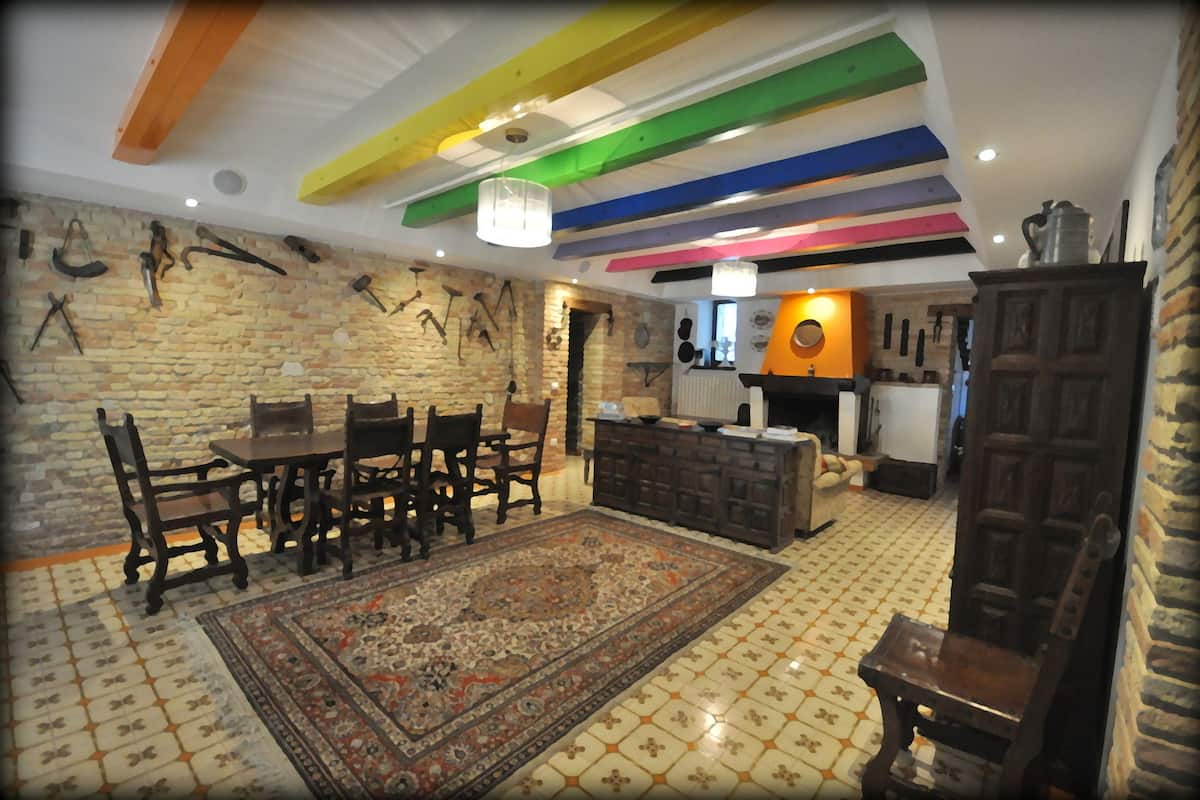 A dining area with a wooden table and chairs, a patterned rug, and a brick wall with mounted cutlery.
