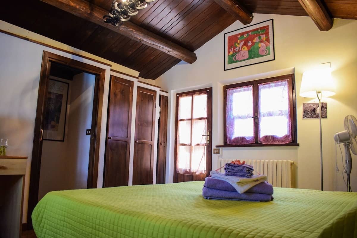 A room with a bed, wooden doors, a window with curtains, a radiator, and a wall-mounted lamp.