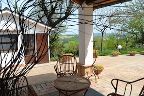 An outdoor patio with a table and chairs, surrounded by potted plants and a view of the countryside.