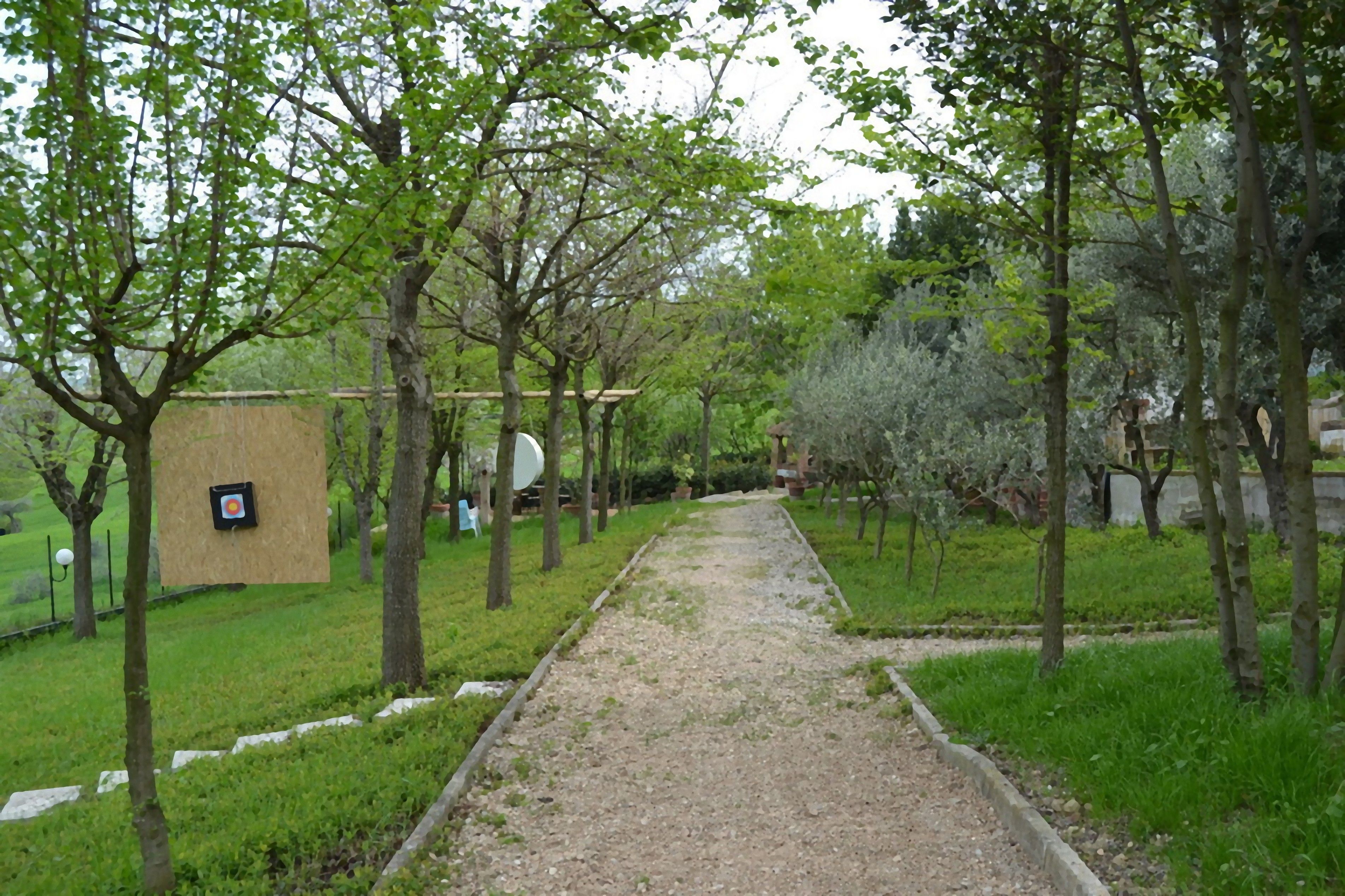 A pathway lined with trees and a small building with a target on the ground.