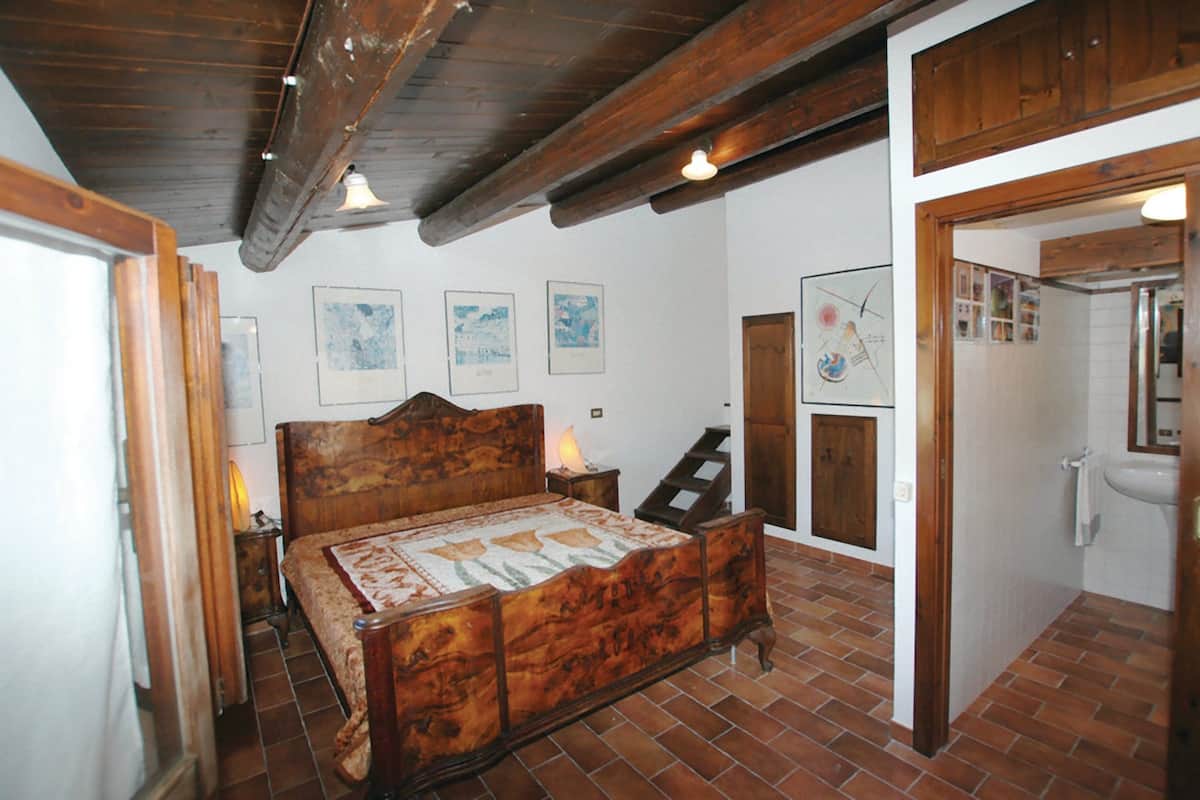 A bedroom with a wooden bed, a nightstand, a lamp, and a door leading to the bathroom.