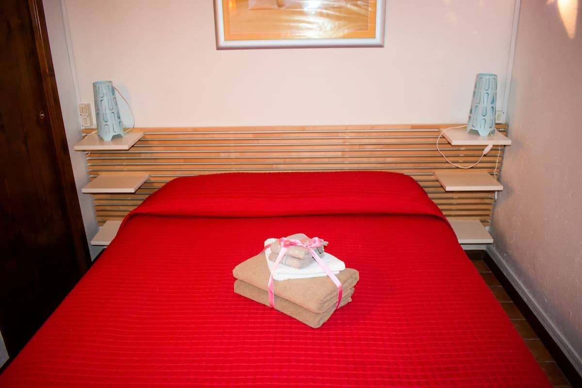 A neatly made bed with a red bedspread and a stack of folded towels on it.