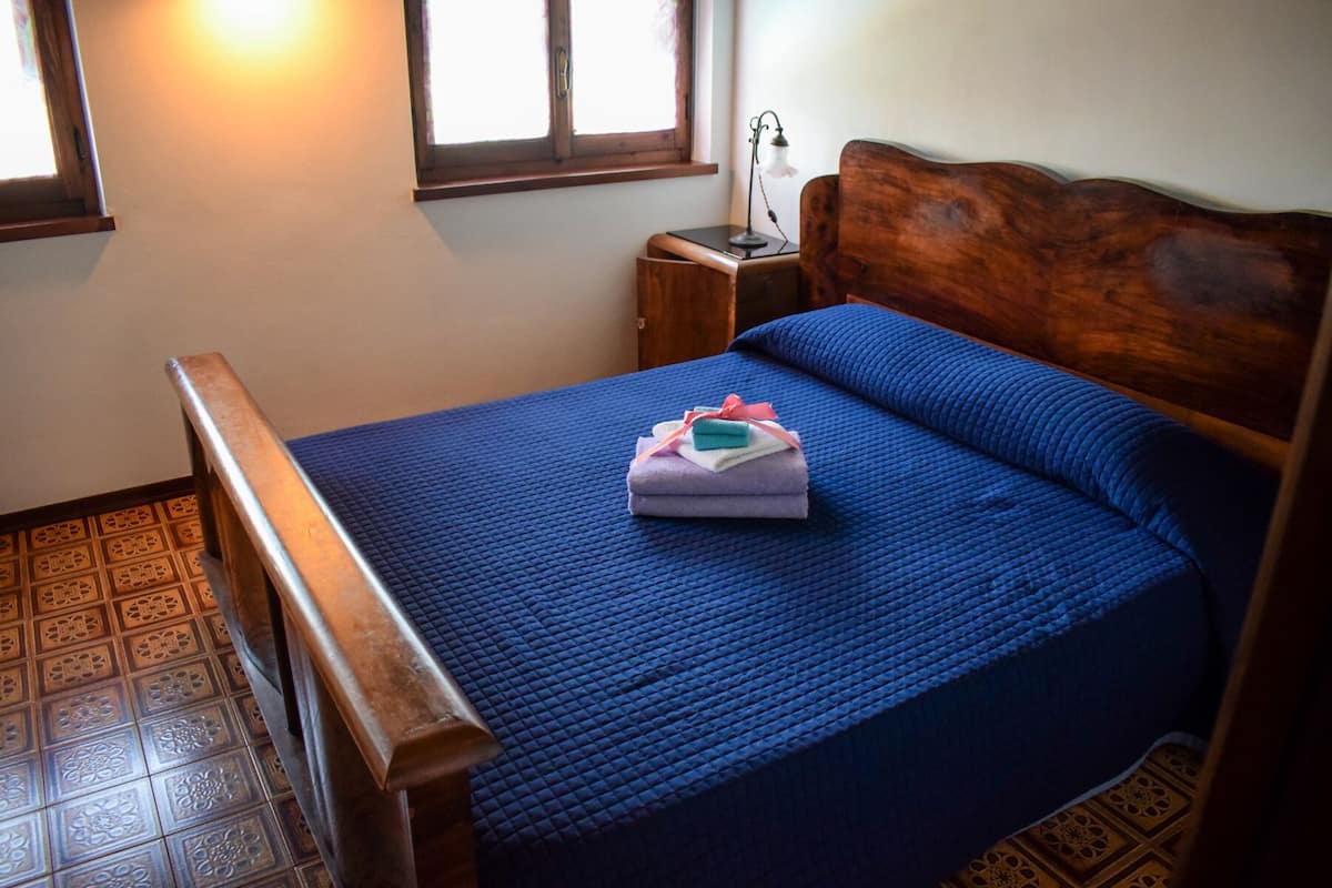 A neatly made bed with a blue bedspread, a wooden headboard, and a small bedside table with a lamp.