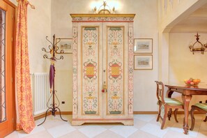 A room with a large, ornate cabinet with decorative panels, a dining table with chairs, and a chandelier.