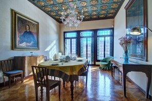 Comedor con una mesa de madera dispuesta para cuatro, una araña y un cuadro grande en la pared.
