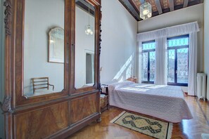 Un dormitorio con un armario grande de madera, una cama con colcha blanca y una ventana con cortinas blancas.