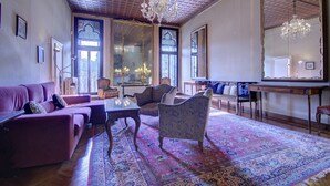 Un salon spacieux doté d’une grande fenêtre, d’un lustre et d’un tapis à motifs.