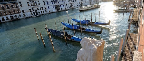 Ein Kanal mit vor Anker liegenden Gondeln, an den Ufern stehende Gebäude und eine Statue im Vordergrund.