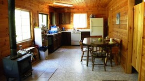 A wooden cabin interior with a kitchen, dining area, and a fireplace. - Woman River Camp (Unorganized Kenora District)