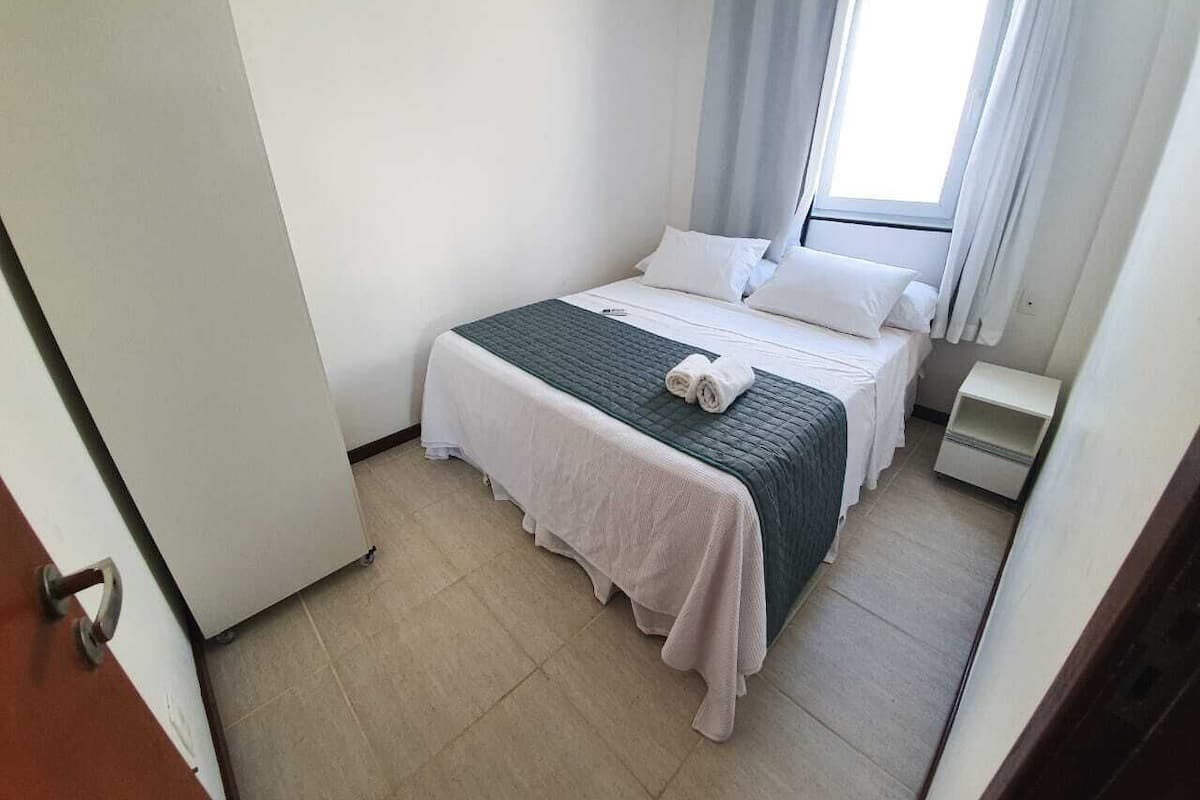 A small, clean room with a bed, a nightstand, and a window with curtains.