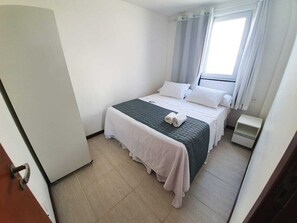 A small, clean room with a bed, a nightstand, and a window with curtains.