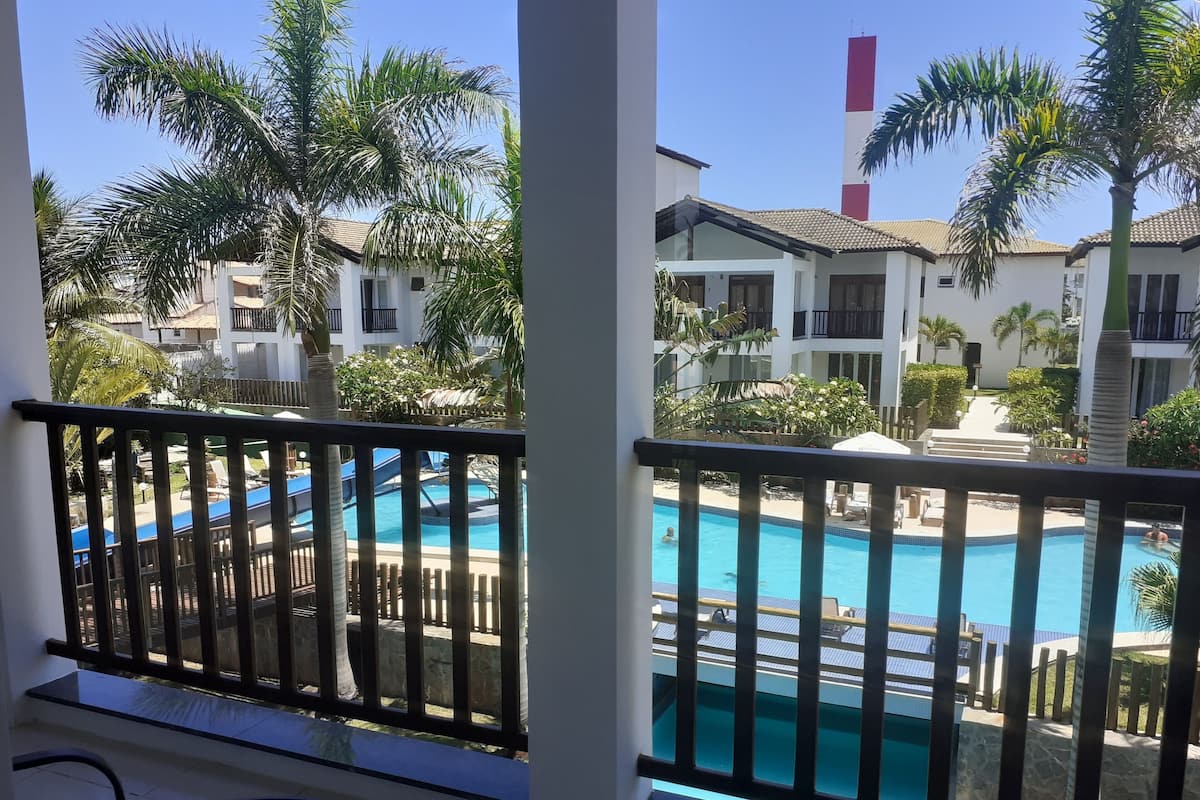 A pool area with a view of a building with balconies and palm trees.