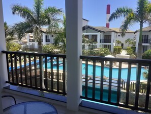 A pool area with a view of a building with balconies and palm trees.