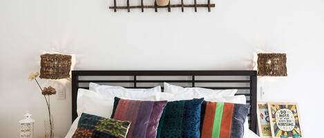 A neatly made bed with multiple pillows, a bedside table with a lamp, and a wall-mounted plant.