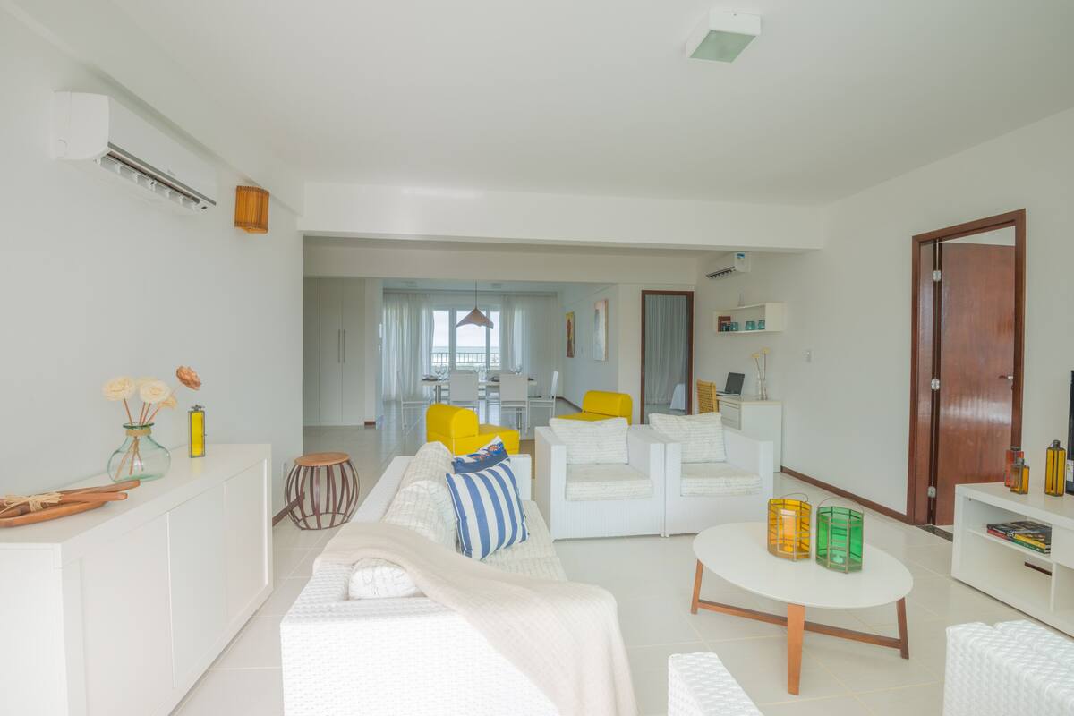A modern living room with a sofa, armchairs, a coffee table, and a dining area in the background.