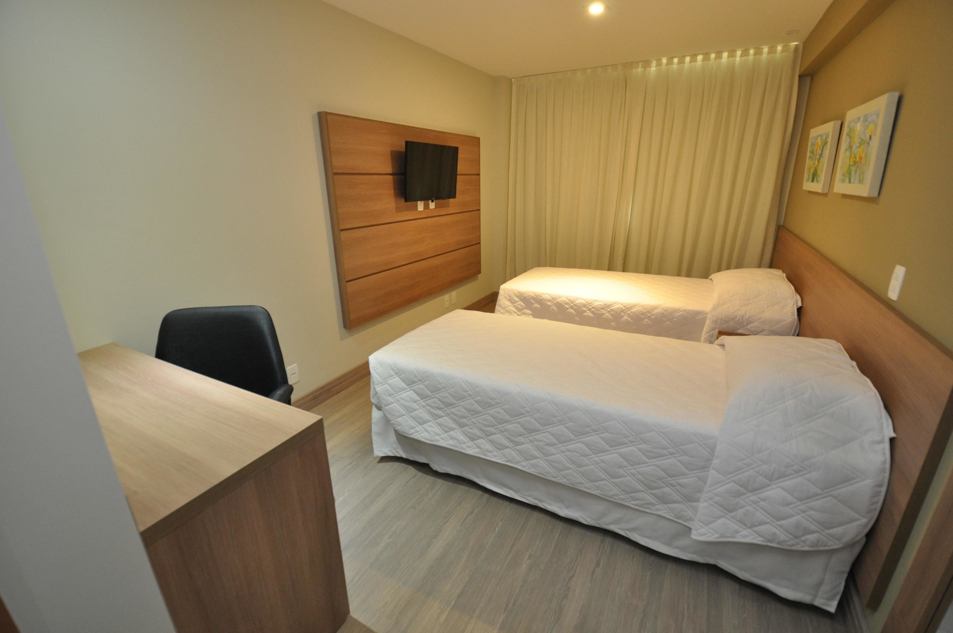 Habitación de hotel con dos camas, un escritorio, una silla, un televisor montado en la pared y cortinas.