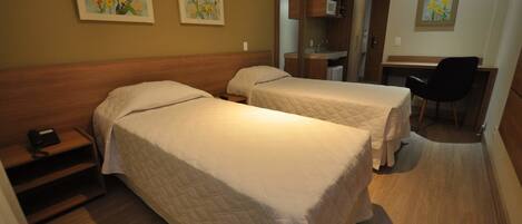 A hotel room with two beds, a desk, a chair, and a small kitchenette.