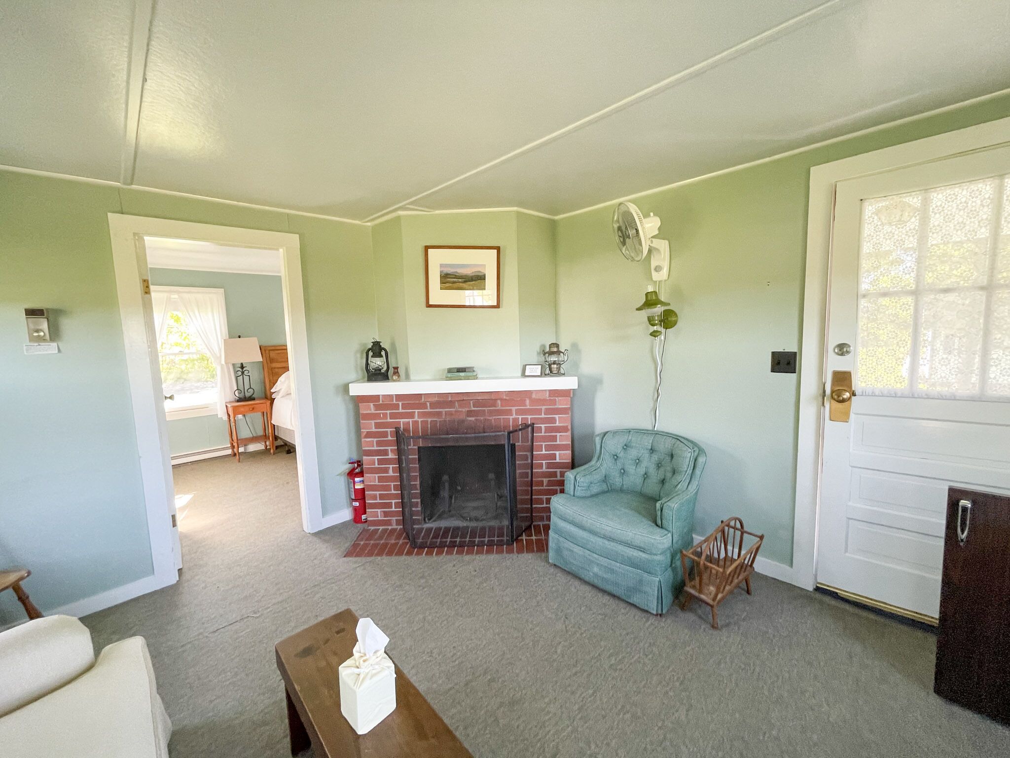 A living room with a fireplace, a blue armchair, a wooden coffee table, and a door with a window.