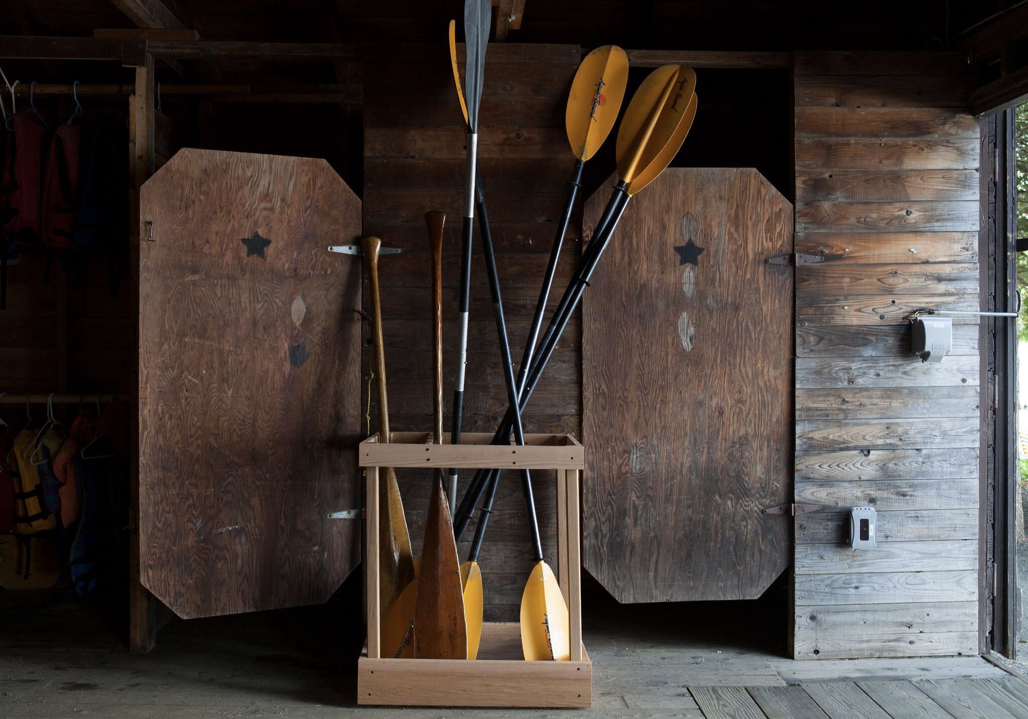 A wooden paddle rack with paddles and a canoe in a rustic cabin.