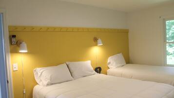A room with two beds, each with white bedding and a headboard. There are two wall-mounted lamps on either side of the beds.