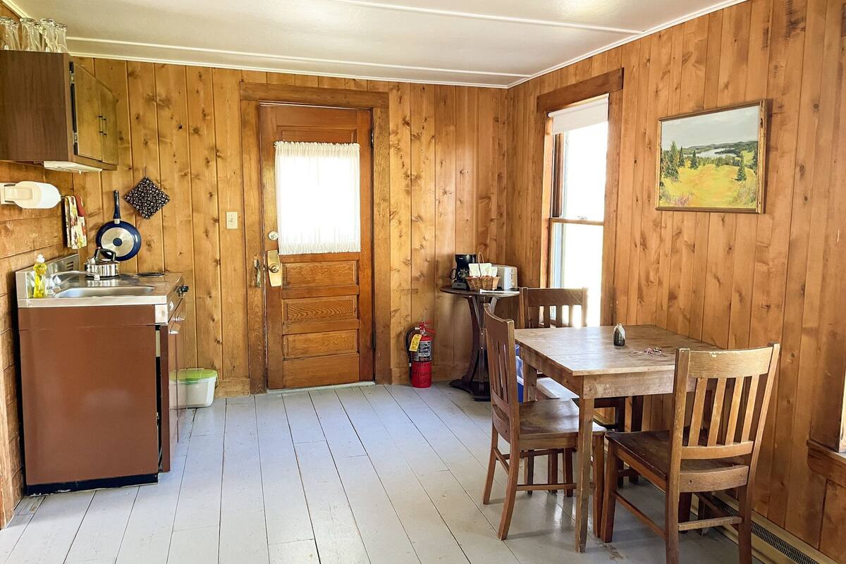 A wooden interior with a kitchen area, dining table, chairs, and a painting on the wall.