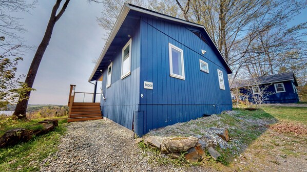 A blue house with a number '8' and the name 'TUDOR' on the side, a wooden staircase leading to a gated entrance, and a small shed in the background. - Highland Lodge (Greensboro)