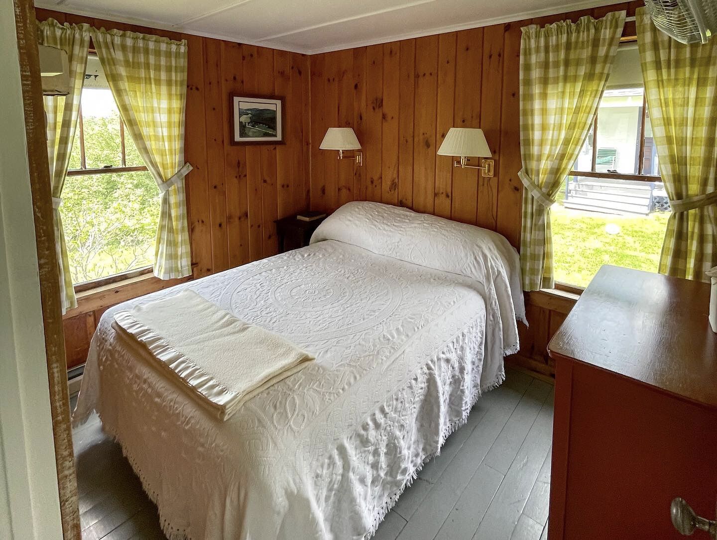 Een slaapkamer met een houten wandpaneel, een bed met een witte dekbedovertrek, twee bedlampjes en een raam met gordijnen.